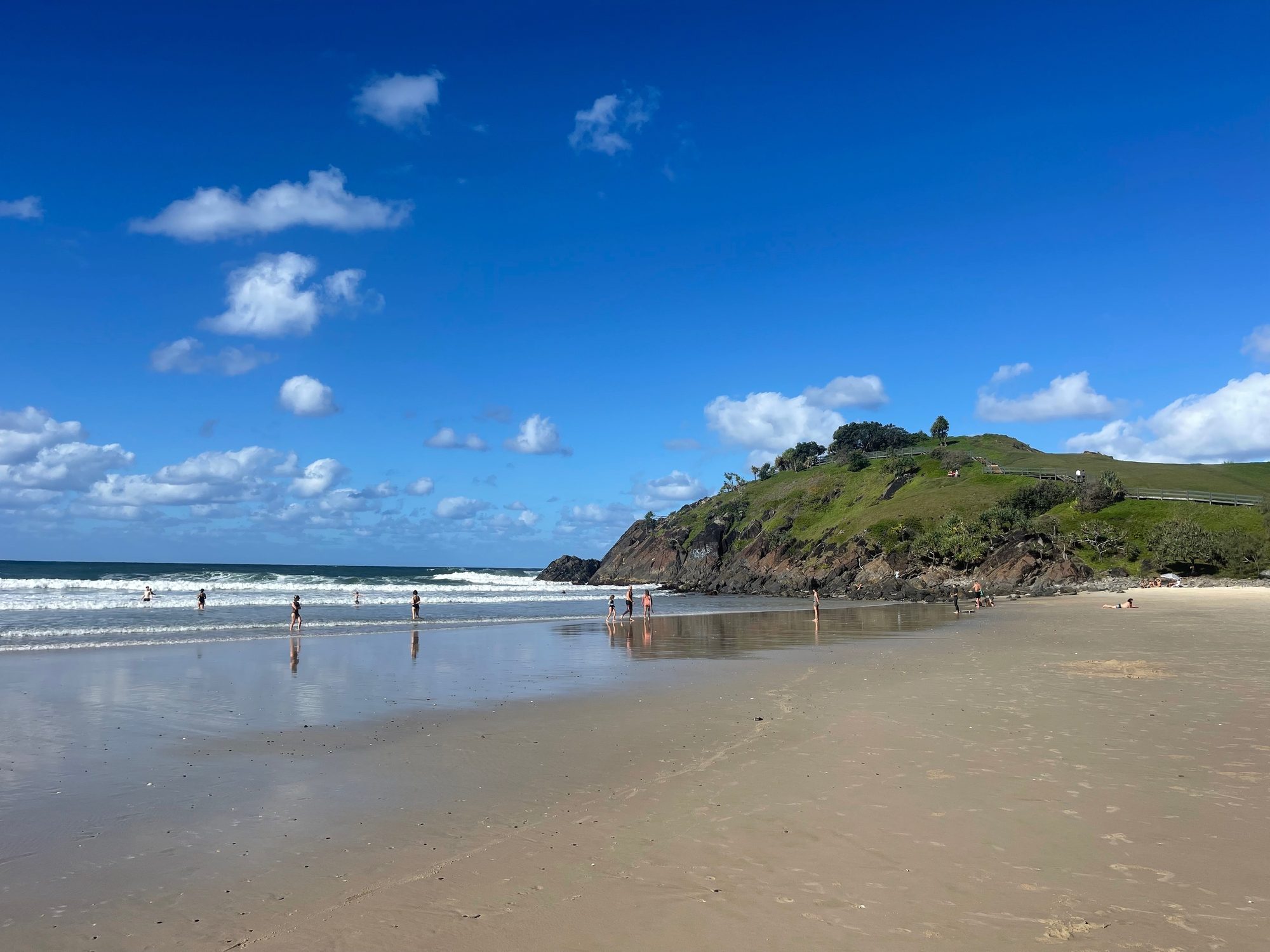 Surf rolling onto a wide sandy beach below a grassy headland
